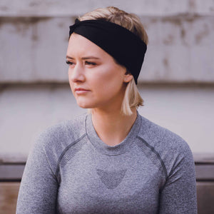 Women wearing a black reversible sports headband sitting outside in activewear