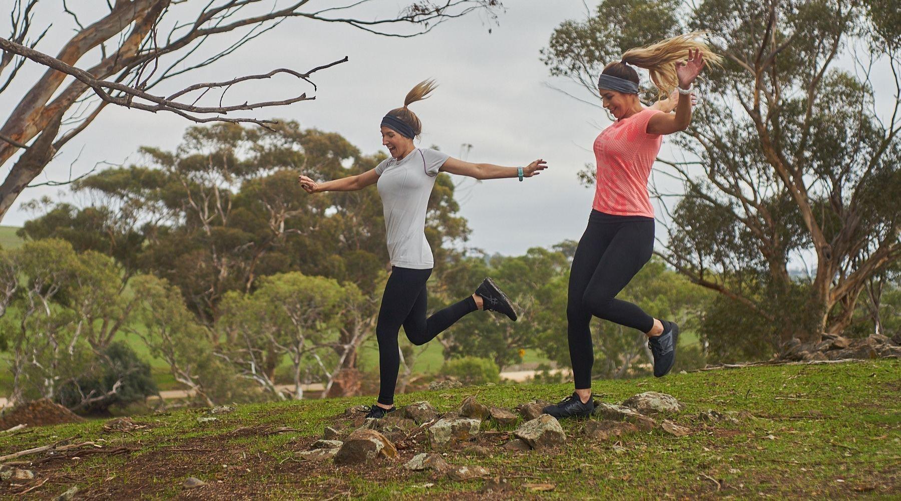 two ladies trail running over rocks with hands in the air wearing technical sports running headbands
