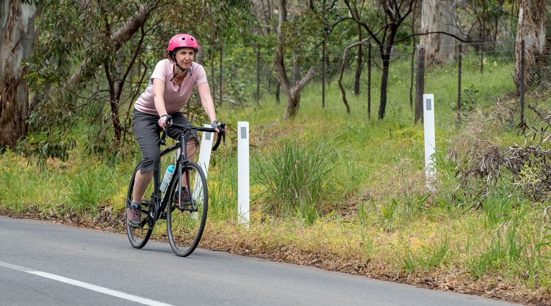 Jo riding bike on road wearing grey helmet friendly sports headband under bright pink helmet