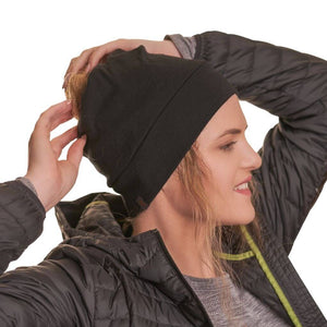 Women wearing sports merino wool beanie with hands on top of beanie adjusting hair smiling to the left