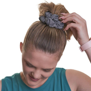 Women wearing grey yoga scrunchie with hand on phigh ponytail gazing at the ground