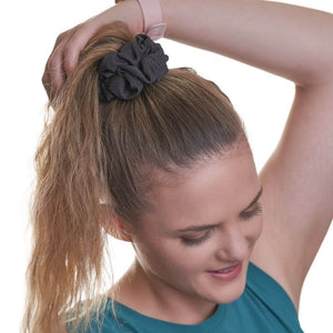 women wearing black sports scrunchie, looking at the ground with hand on ponytail