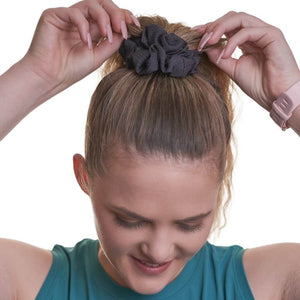 Women wearing black gym scrunchie looking to the ground with both hands holding ponytail.